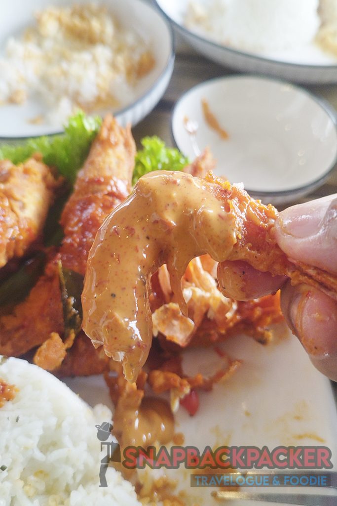 a hand holding a piece of spicy crispy fried prawn dipped in buttermilk sauce